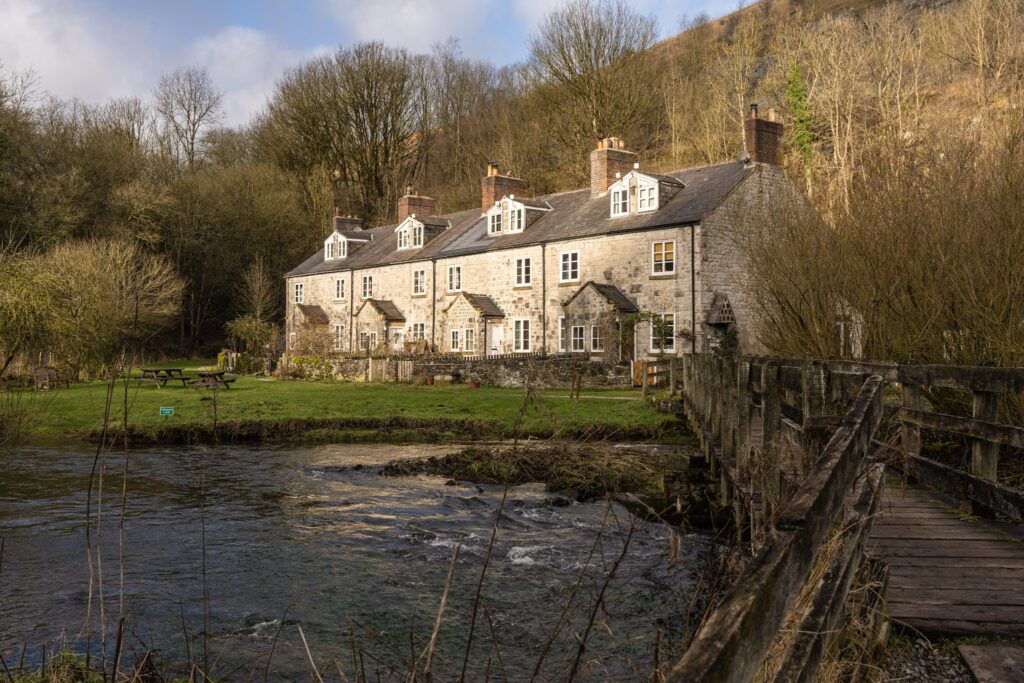 Row of pretty Derbyshire cottages alongside the river wye with wooden bridge going over