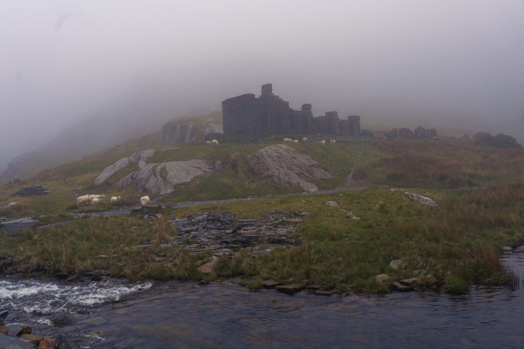 Abandoned buildings at Cmorthin quarry on the hill in the mist, stream in the foreground