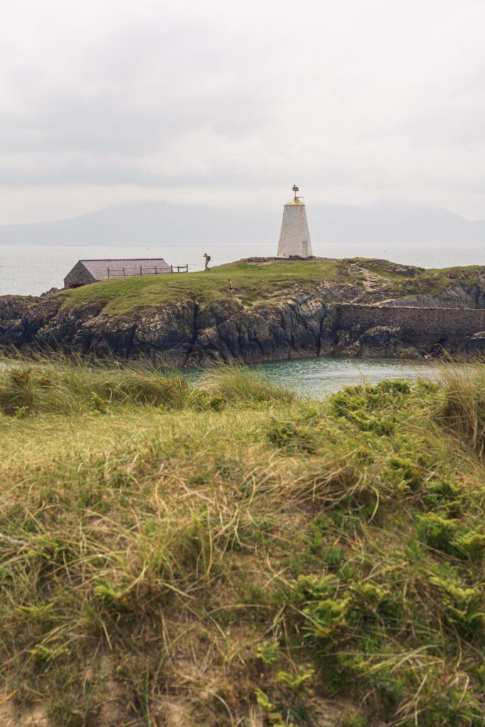 lighthouse and boat house behind a sea inlet and sandy grass bank