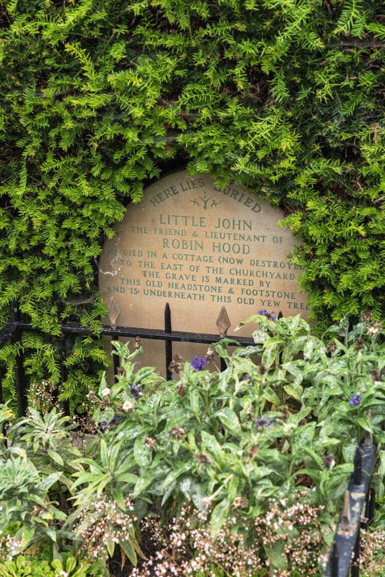 Little Johns Grave with green foliage all around the headstone and iron bars around the grave
