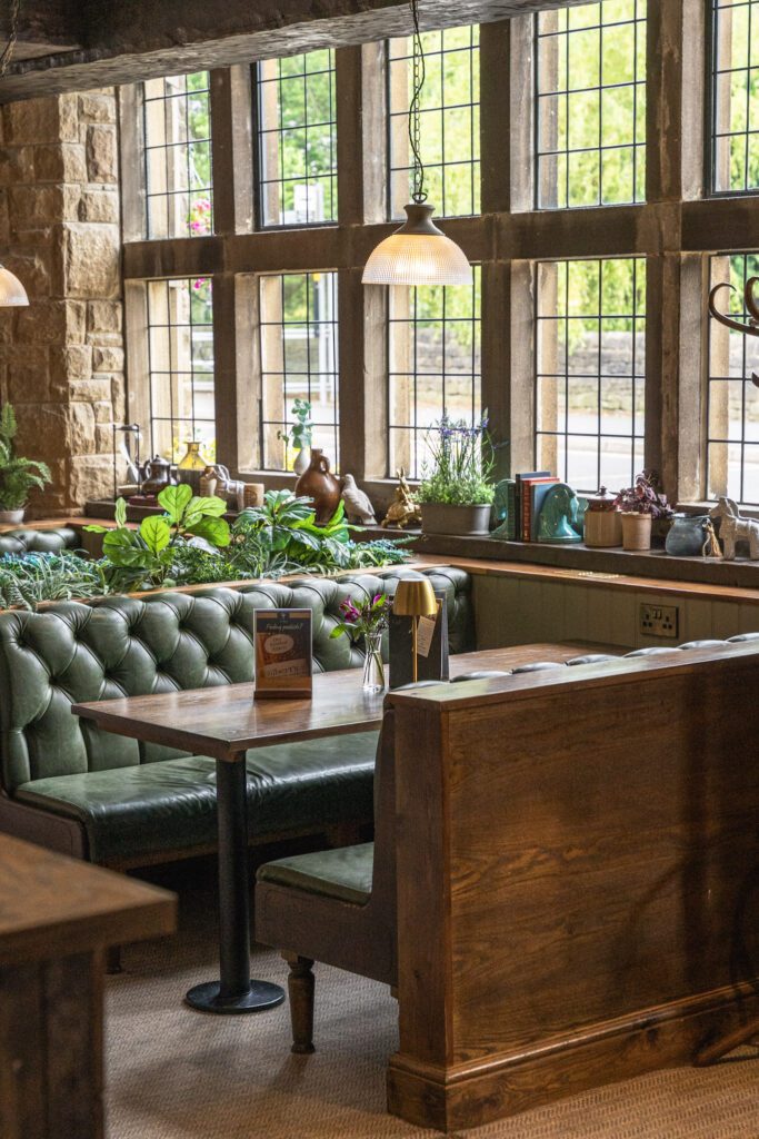 Wooden booth seating with green leather covering, large leaded windows to one side
