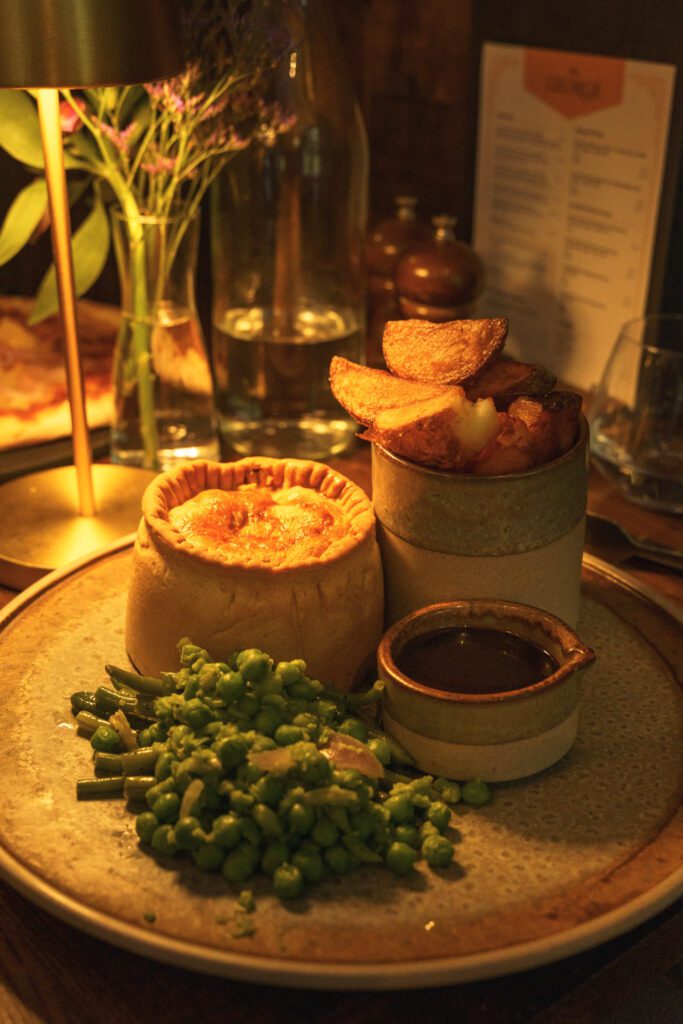 Homemade individual pie, chunky chips in a pot with garden peas and gravy, mood lighting, menu in the background