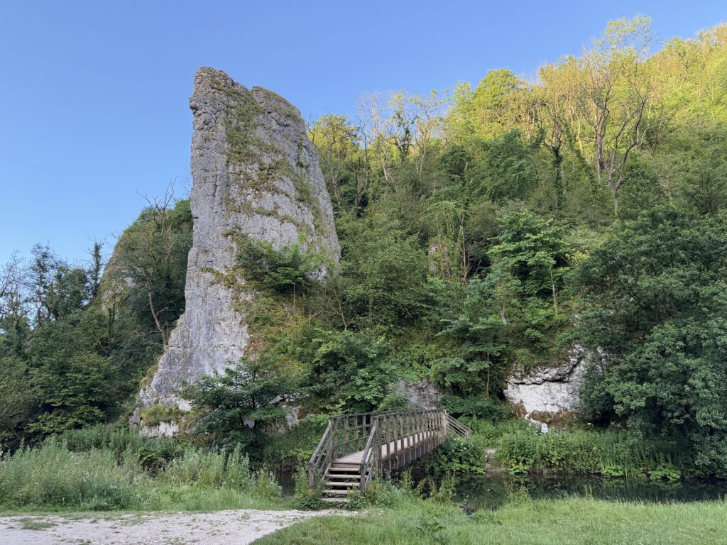 Large limestone rock standing alone on the river Dove with a wooden bridge crossing the river towards it