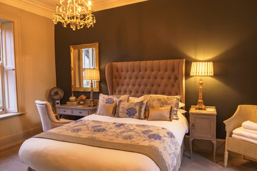 Double bed in a beautifully decorated room with gold mirror, bedside lights and other bedroom furniture