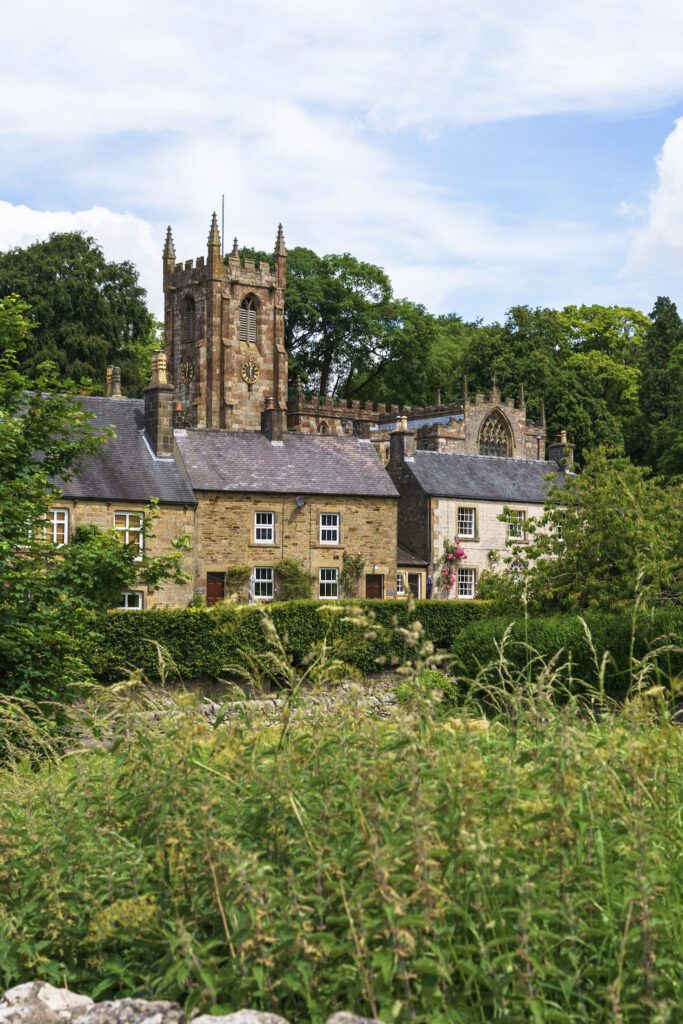 Hartington church from the next street above dry stone walling and wild nettles