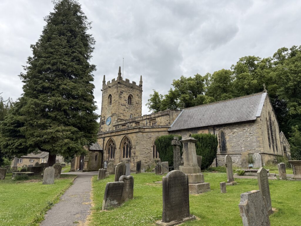 Eyam Church with old gravestones in the grounds and large trees