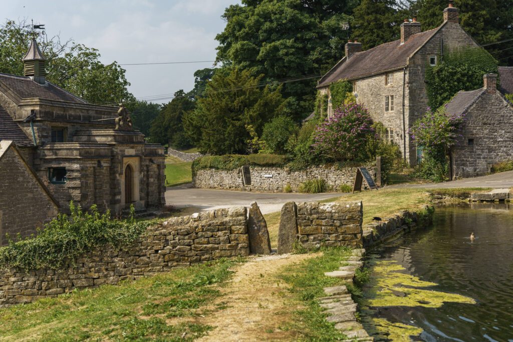 Tissington duck pond with beautiful stone houses in the background and a squeeze stile