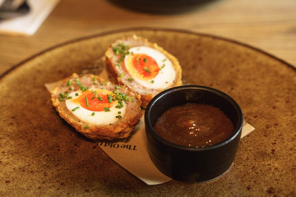Scotch Egg and homemade ketchup on branded paper plated and garnished with chives
