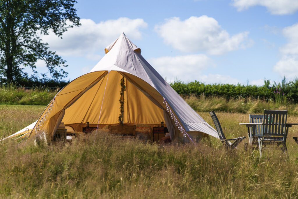 Tipi surrounded by meadowland on our off grid campsite with table and chairs