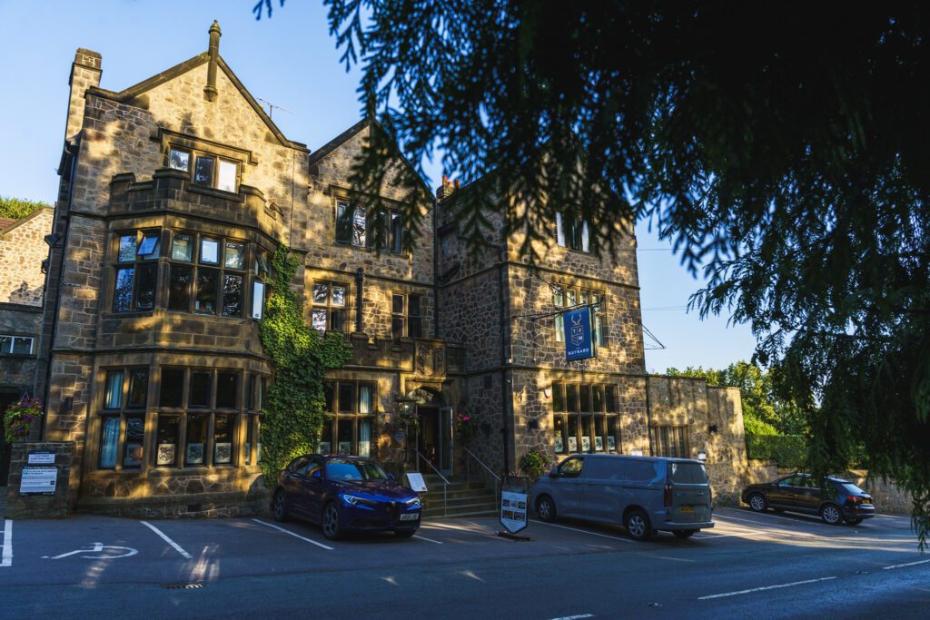 The Maynard Exterior, a beautiful stone traditional building with ivy growing up the front and cars parked outside