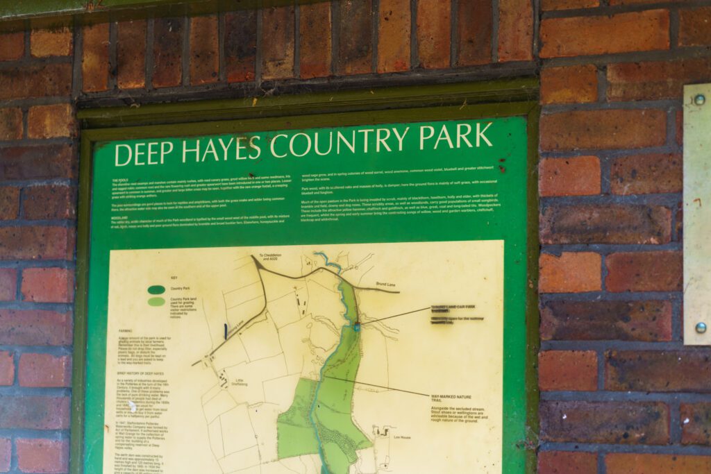 The green entrance information board for Deep Hayes Country Park, mounted on a brick wall with a trail map.