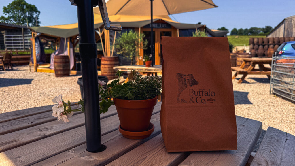 A Buffalo and Co Kitchen paper bag on a table in the outdoor seating area at Oakleys Farm.