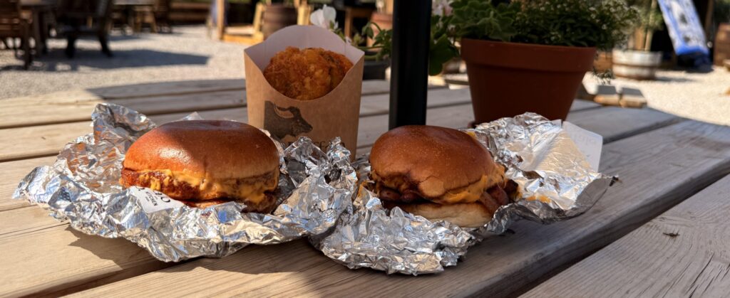 A sausage and bacon bap with hash browns on a table in the outdoor seating area at Oakleys Farm.