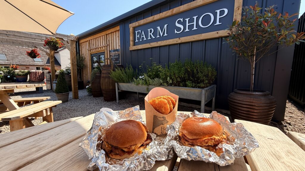 The Farm Shop building sign at Oakleys Farm, seen from the outdoor seating area with chips on the table.