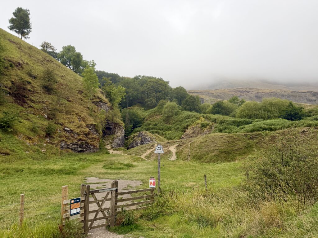 Odin Mine entrance behind a fence line and cloud covered hills behind